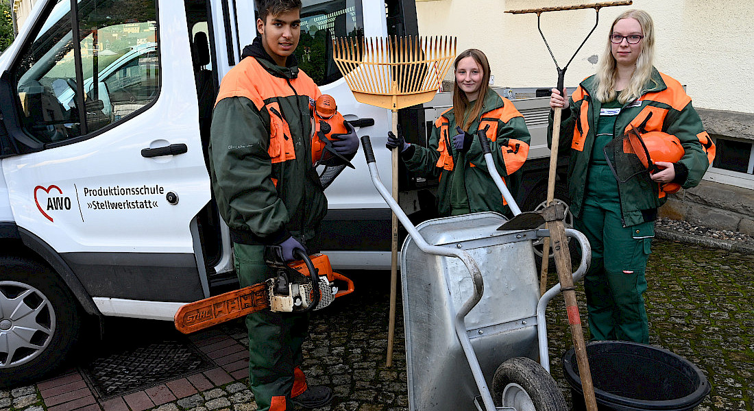 Jugendliche in Arbeitskleidung stehen vor einem Transporter mit Gartengeräten.