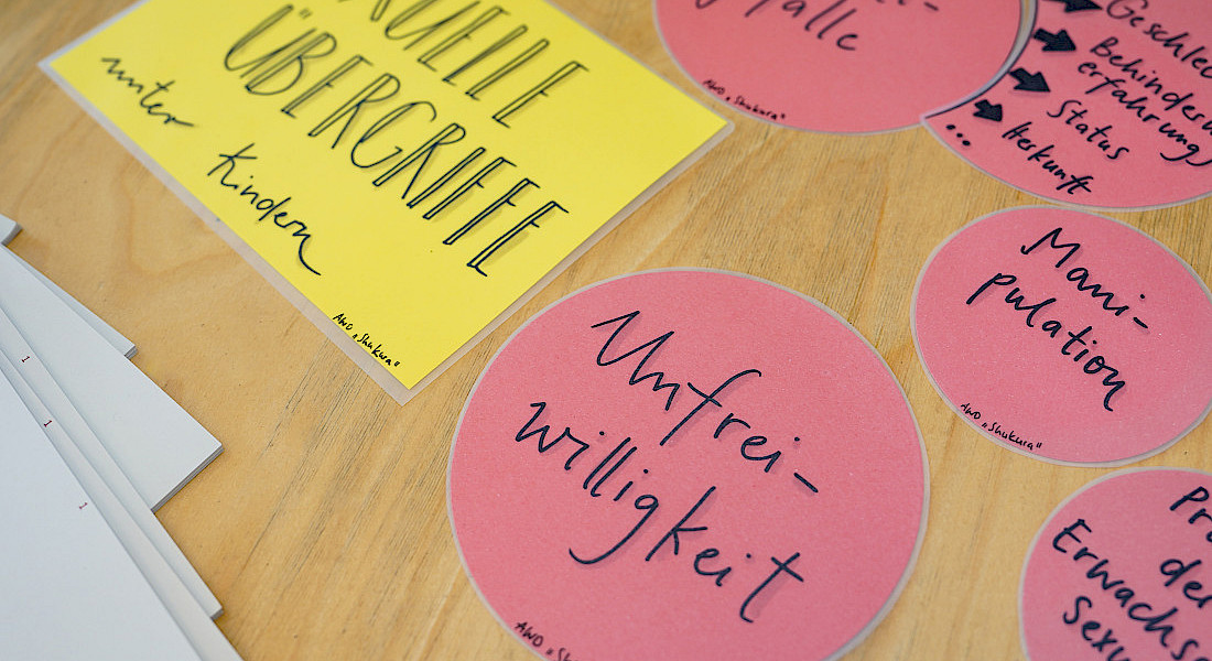Auf einem Tisch liegen gelbe und rosa Zettel mit den Aufschriften 