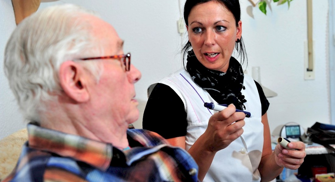 Zwei Personen sitzen in der Stube, die Schwester bereit die Gabe von Medikamenten mit einem Pen vor.