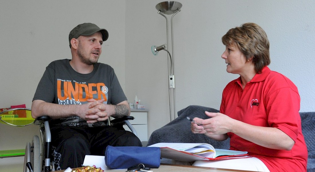 Fachkraft im Gespräch mit Person im Rollstuhl.