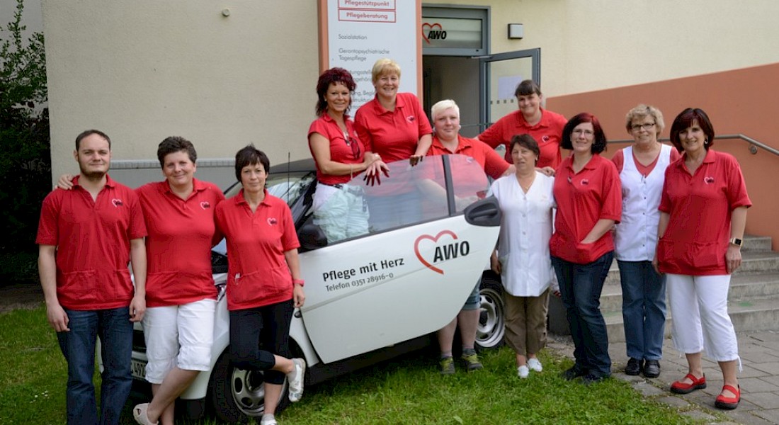 Teamfoto mit elf Personen an einem AWO-Auto vor Eingangsbereich.