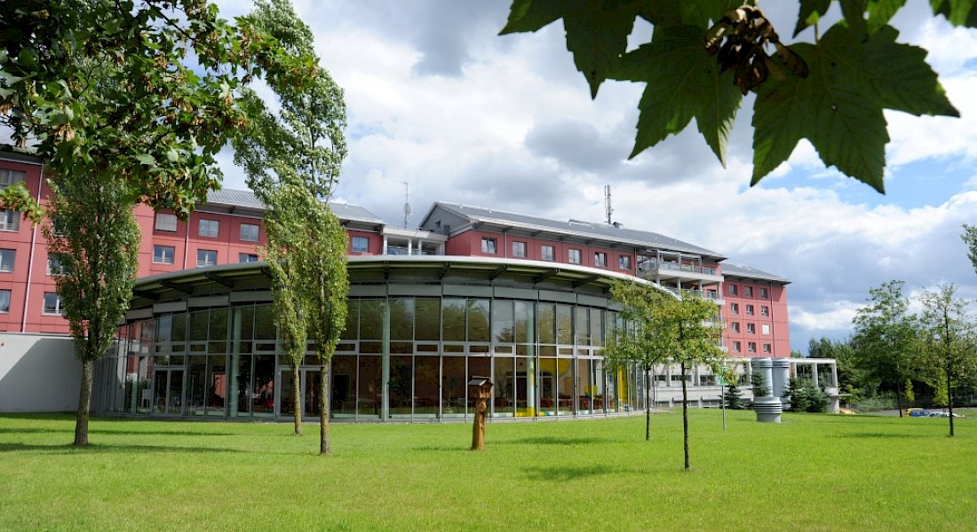 Blick in den Park und auf den gläsernen Speise- und Veranstaltungssaal einer Pflegeeinrichtung.