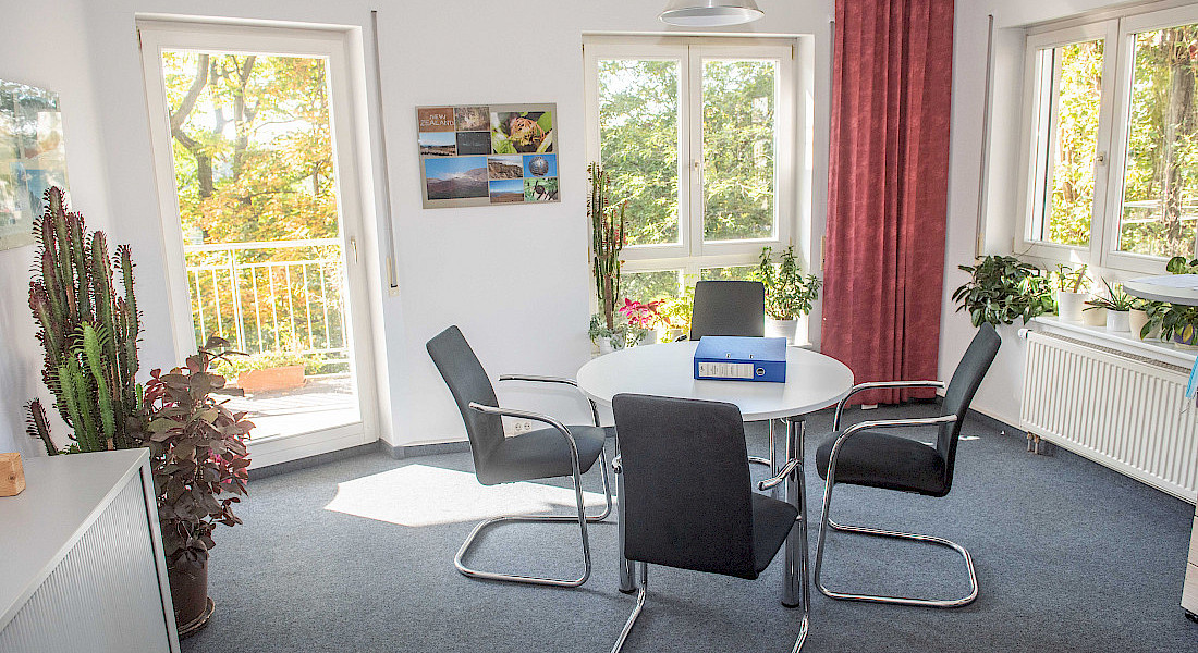 Ein heller Besprechungsraum mit vier Stühlen, einem runden Tisch und mehreren Pflanzen.